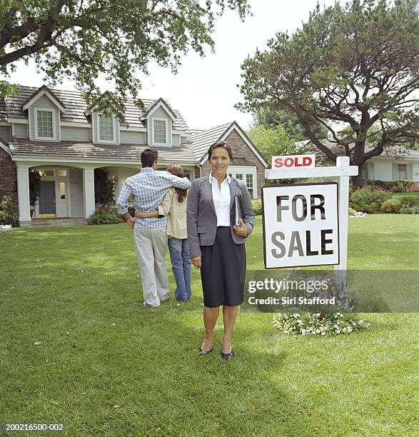 real estate agent standing in front of house with 'sold' sign - estate agent sign stockfoto's en -beelden