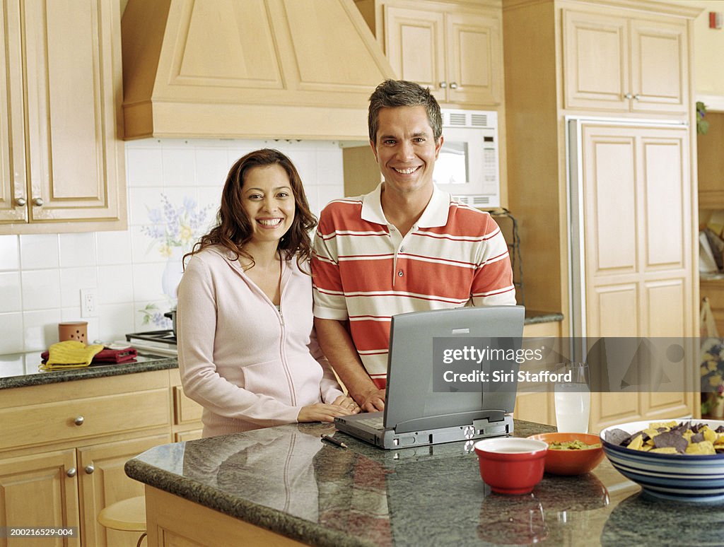 Coppia in piedi in cucina, computer portatile sul banco