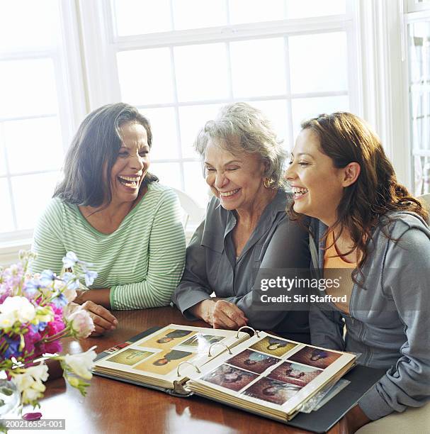 three generation family looking at old photographs, laughing - erwachsene kinder stock-fotos und bilder