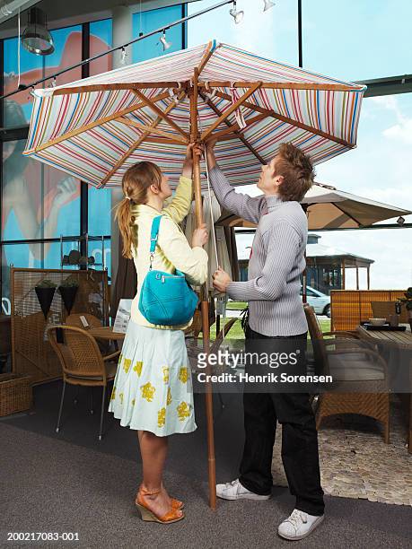 couple opening parasol at garden centre - patio umbrella stock pictures, royalty-free photos & images