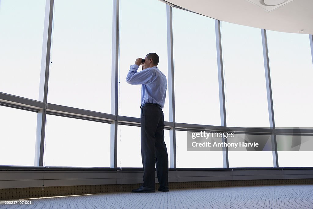 Man looking through binoculars out of office window, low angle view