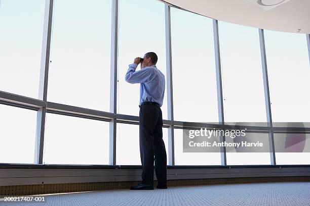 man looking through binoculars out of office window, low angle view - looking through binoculars stock pictures, royalty-free photos & images