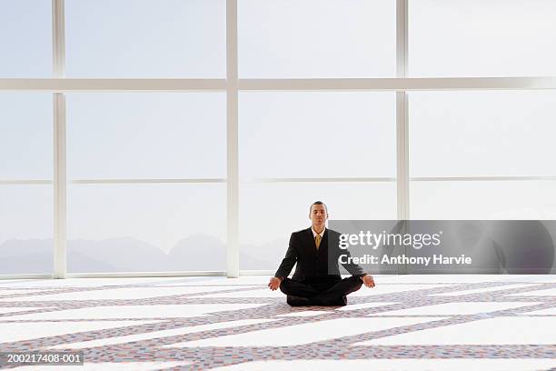 man meditating, sitting cross-legged in office, eyes closed - sunny office stock pictures, royalty-free photos & images