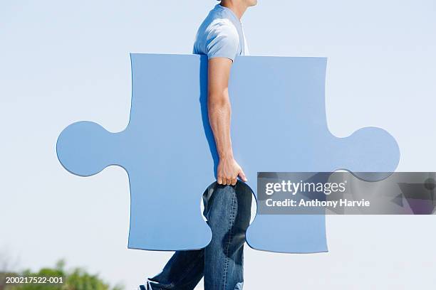 man carrying giant jigsaw piece under arm, side view - big puzzle photos et images de collection