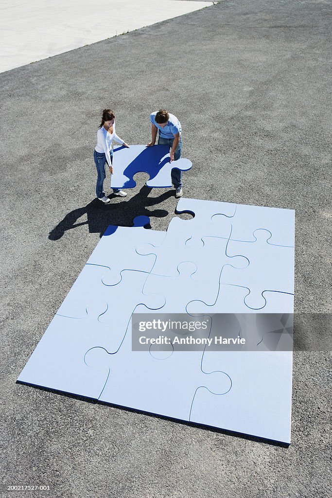 Couple placing last piece in giant jigsaw puzzle, elevated view