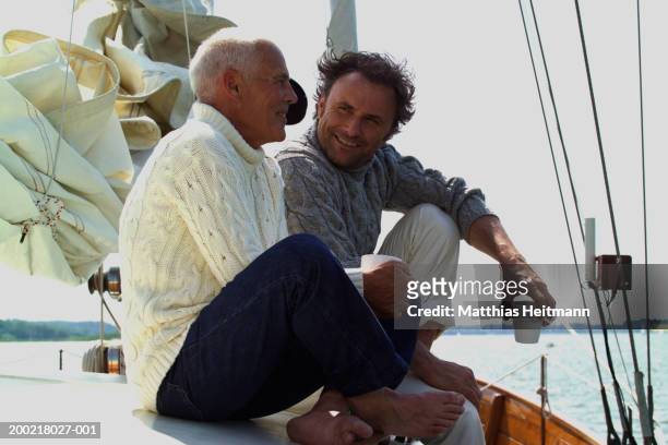two men holding coffee cups sitting on yacht, smiling - father son sailing stock-fotos und bilder