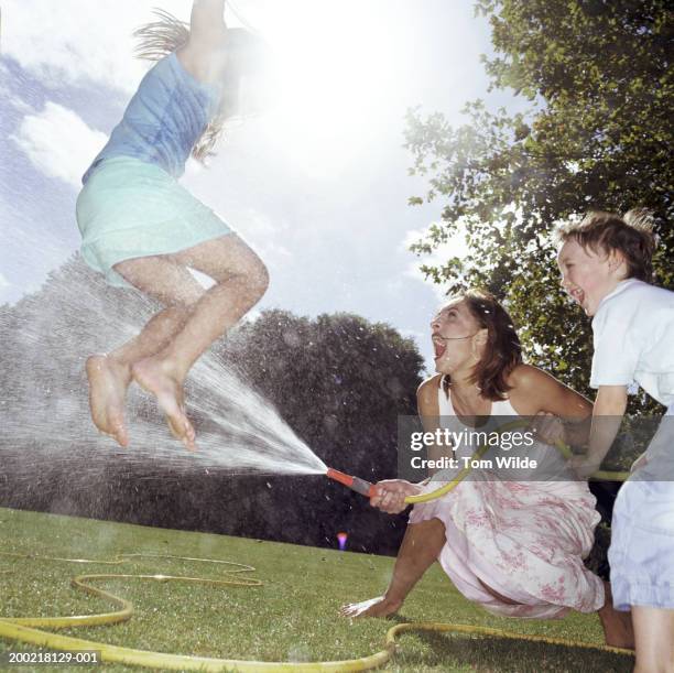 young woman playing with boy and girl (6-10) in backyard - two kids playing with hose stock pictures, royalty-free photos & images