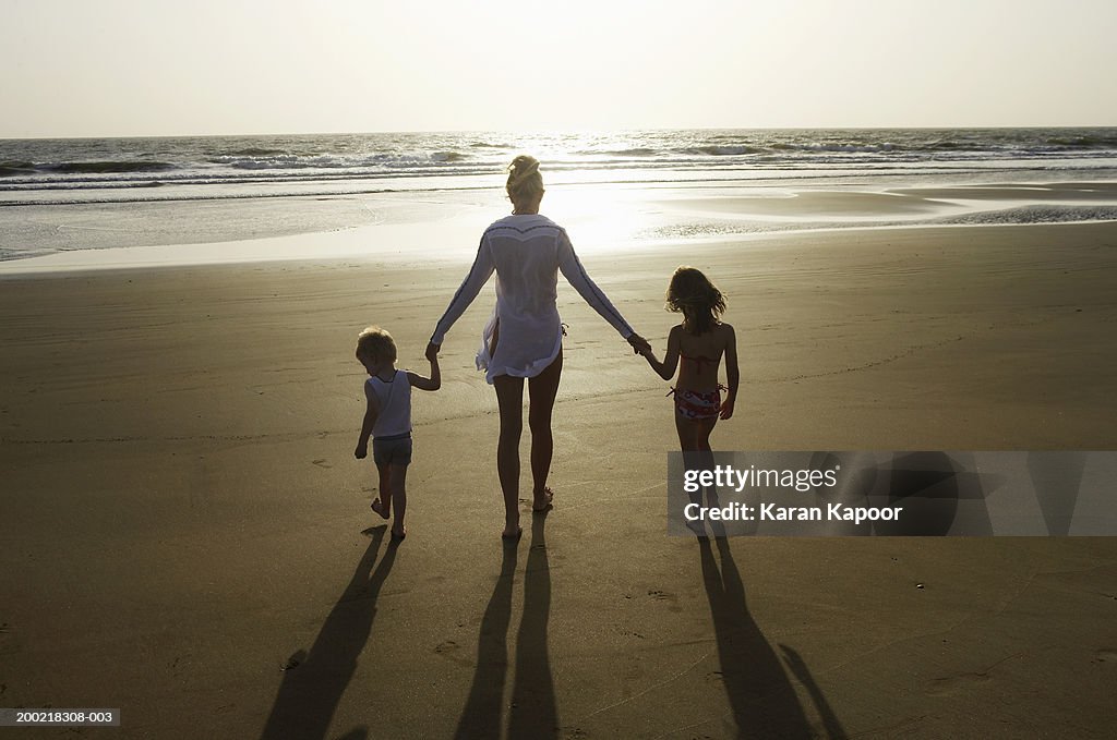 Mother, daughter and son (3-7) holding hands on beach, rear view