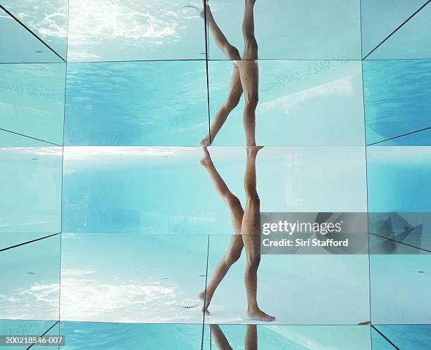 Woman walking in swimming pool, legs reflected on glass