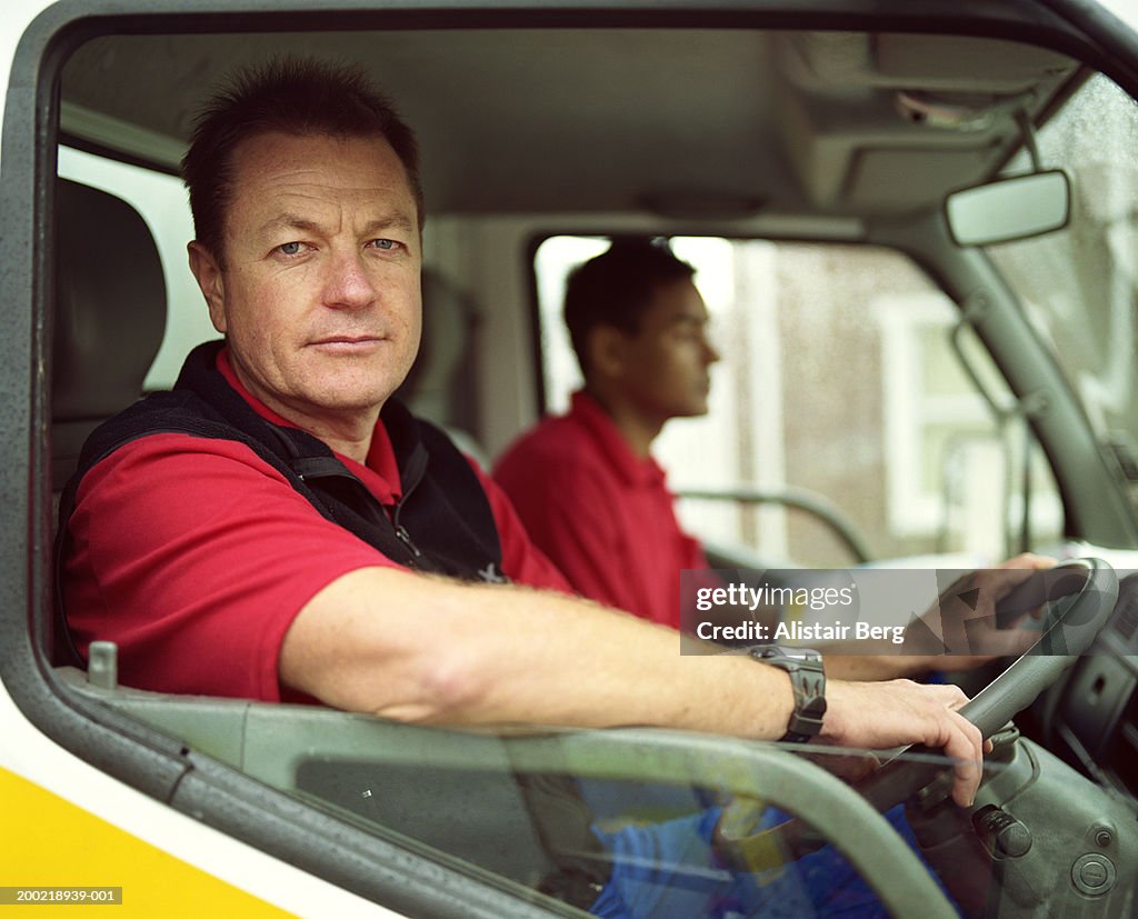 Mature delivery man at wheel of truck with colleague, portrait