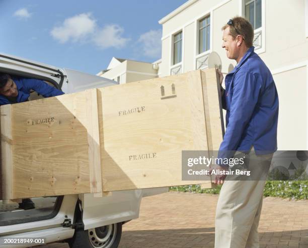 two removal men unloading crate from van - fragilità foto e immagini stock