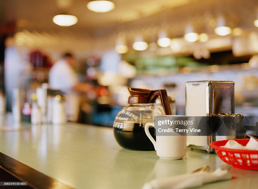 Diner counter top with coffee pot and cup next to napkin dispenser