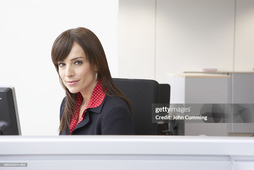 Businesswoman seated at desk in office, smiling, portrait