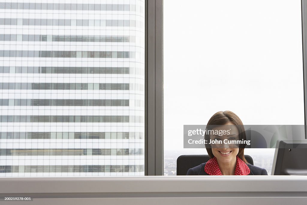 Businesswoman at desk in office, smiling, portrait