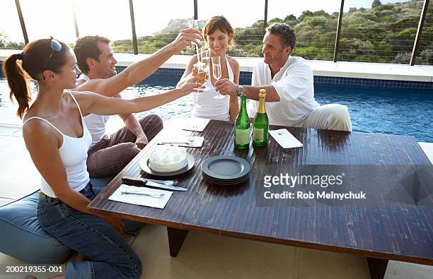 four adults toasting with champagne at table beside swimming pool - four people foto e immagini stock