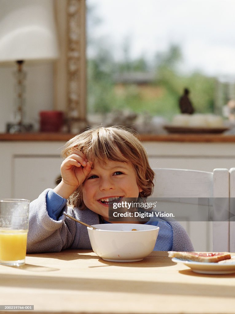 Boy (4-6) having breakfast in kitchen, laughing