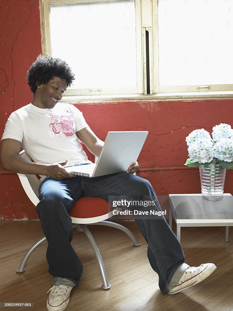 Young man in chair with laptop, smiling