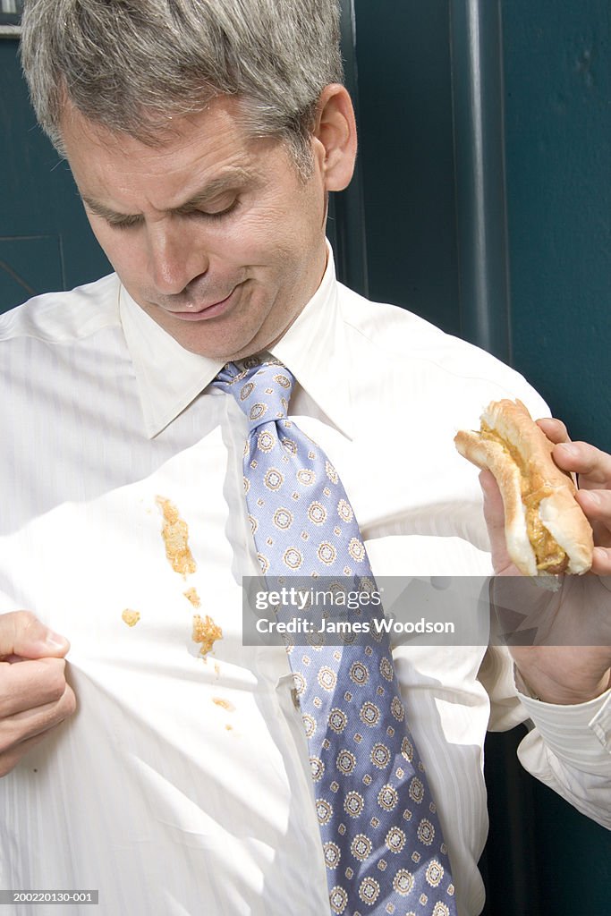 Businessman outdoors, hotdog sauces spilt on shirt, close-up