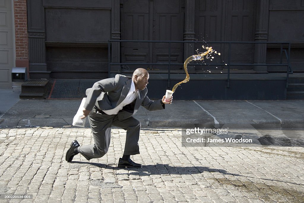 Businessman outdoors, spilling cup of coffee on pavement, side view