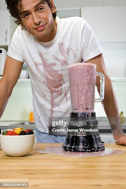 young man in kitchen, by blender, smoothie spilt on shirt, portrait - blender foto e immagini stock