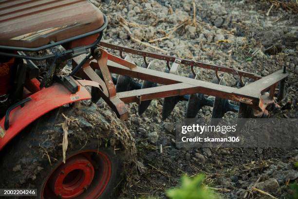 red tractor with tilling attachment working the soil, turning up earth and crop residue in a cultivated field. - plow stock pictures, royalty-free photos & images