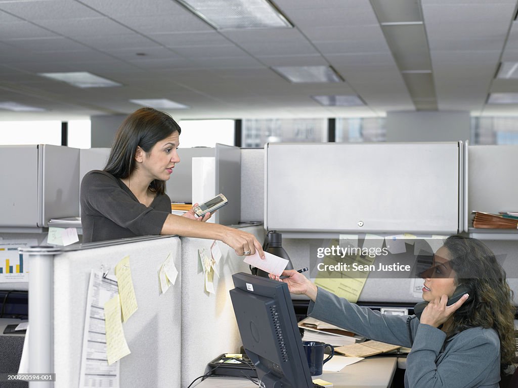 Businesswomen passing phone message between cubicles, side view