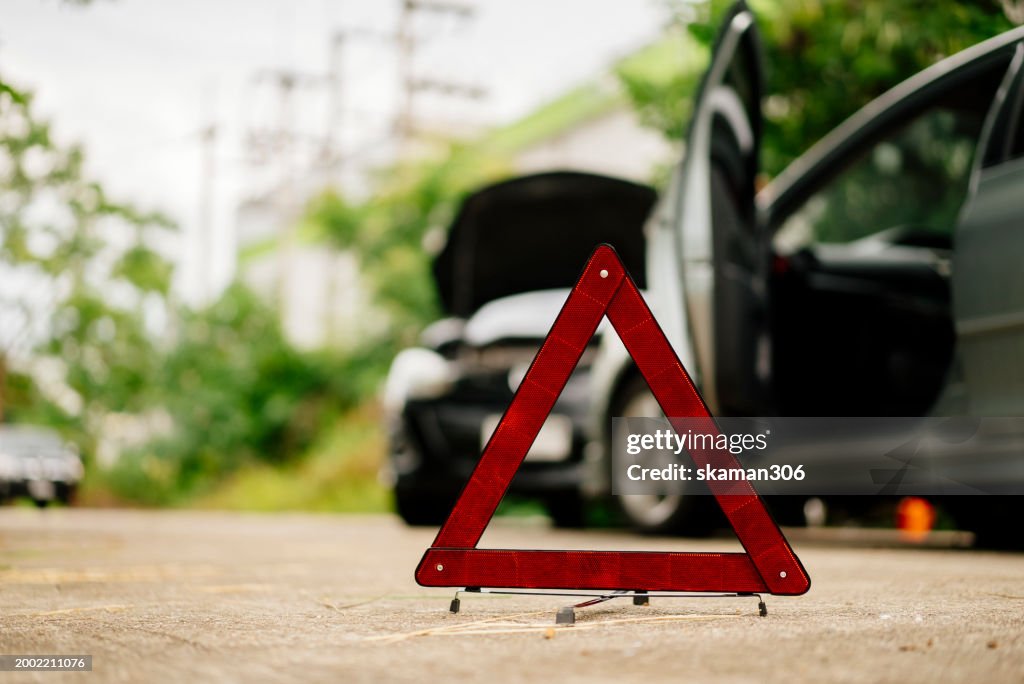 Insurance adjuster claim a Man in a safety vest setting up a red warning triangle by a car, indicating a breakdown or roadside emergency.