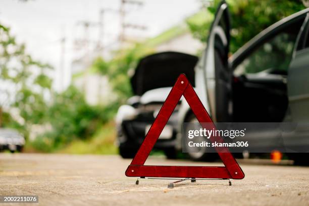 insurance adjuster claim a man in a safety vest setting up a red warning triangle by a car, indicating a breakdown or roadside emergency. - siniestro fotografías e imágenes de stock