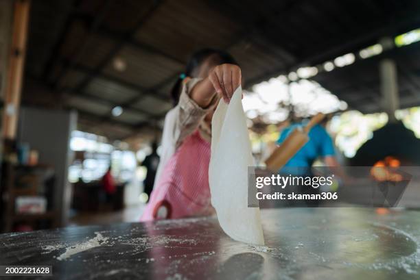 a focused little girl with a rolling pin works on flattening dough in a cooking class, wearing a cute bucket hat and apron. - asian pin up girls stockfoto's en -beelden