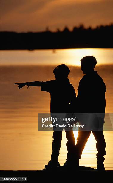 Two Boys Standing By Lake At Sunset Side View High-Res Stock Photo