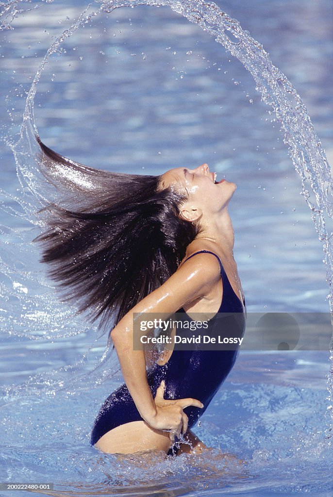Young woman throwing head back in pool, side view