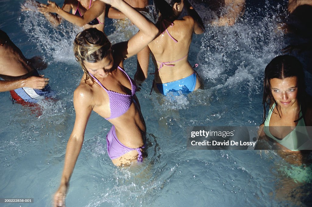 Medium group of young adults dancing in pool at night, elevated view, waist up