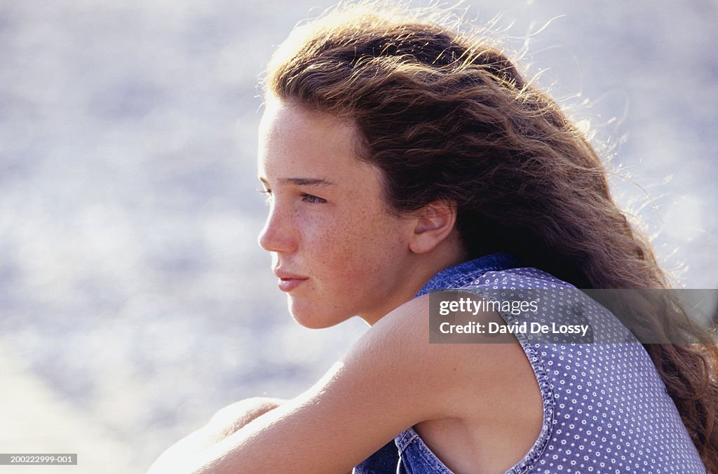 Teenage girl (16-17) sitting at beach, side view