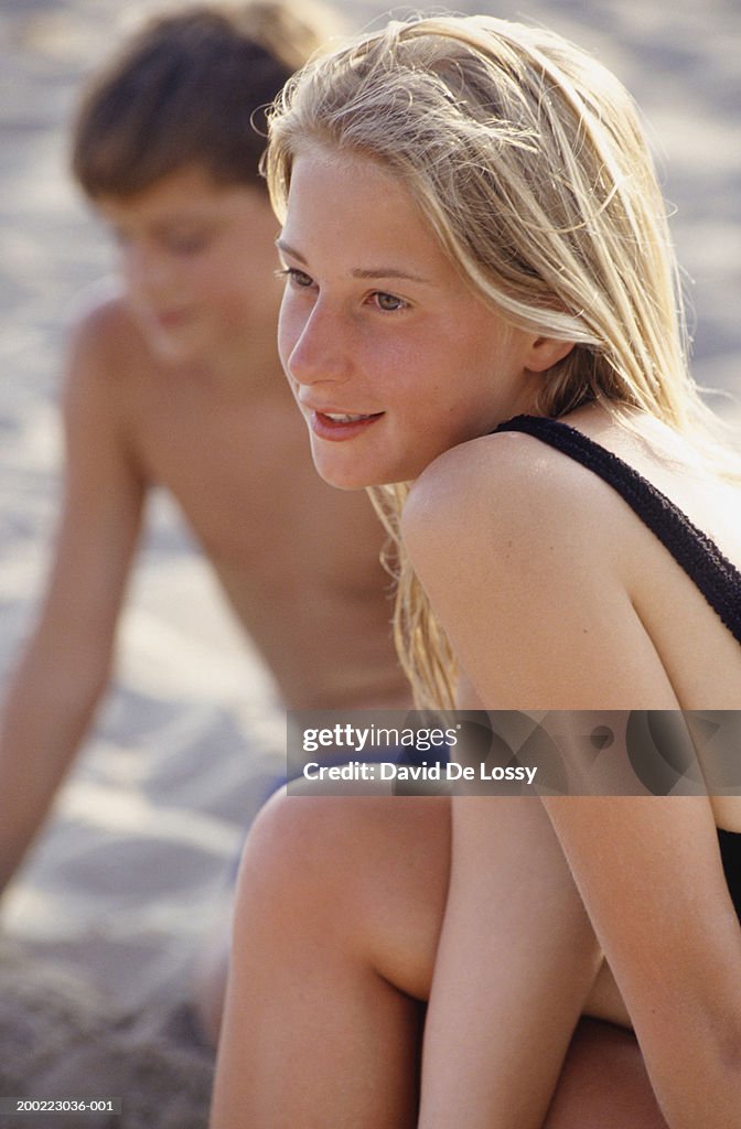 Teenage girl (13-14) and  teenage boy sitting on beach