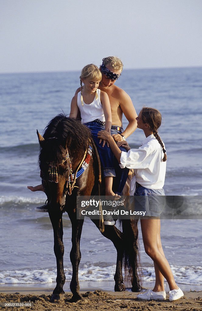 Family at seaside, man and girl (8-9) riding horse