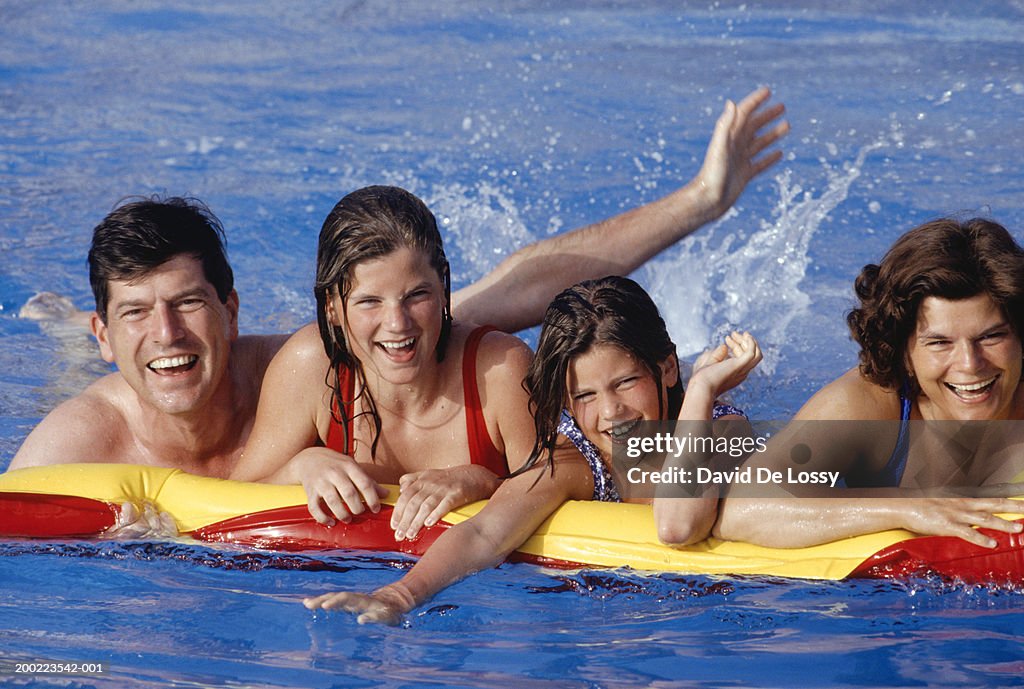 Two mature adults and two girls (12-13) on raft in pool, portrait