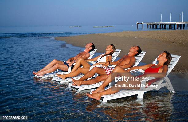 two couples lying on sunloungers in ocean - beach seat stock pictures, royalty-free photos & images