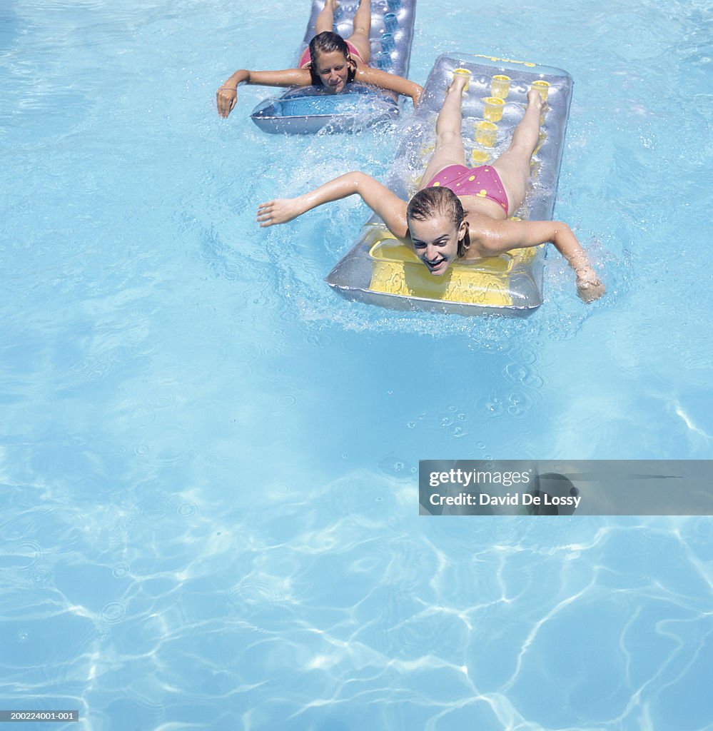 Two teenage girls (16-17) floating face down on airbeds in pool, elevated view