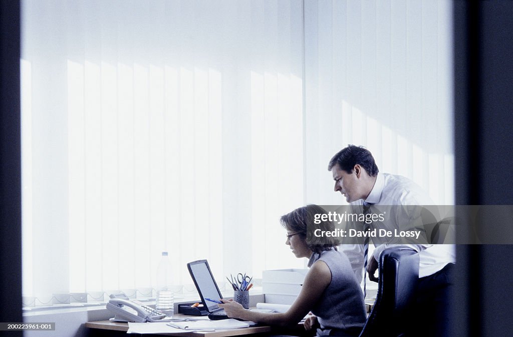 Businessman and secretary using laptop in office, side view