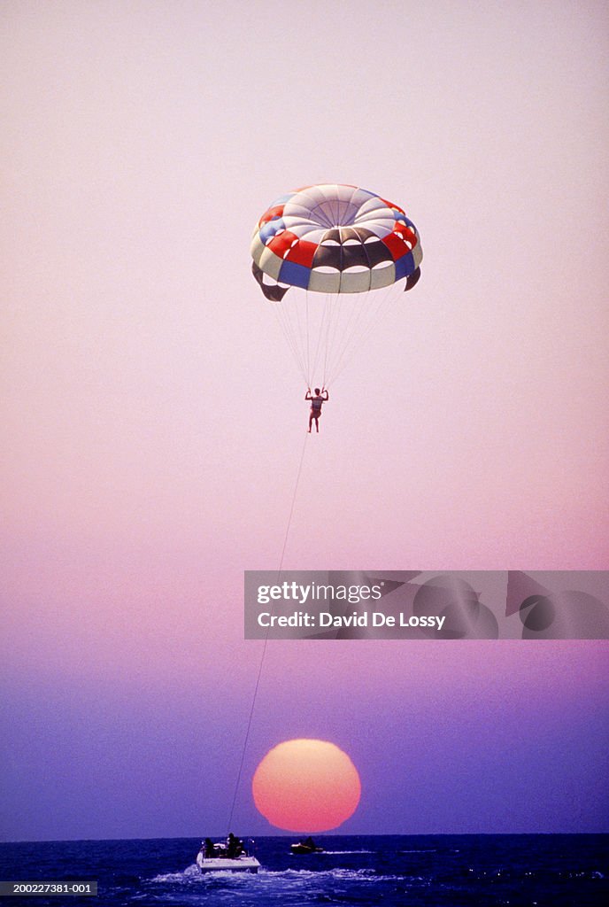 Man parachuting over sea at sunset,