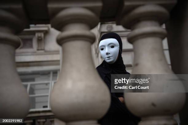 Protester wearing a mask looks through balustrades during an Amnesty International UK demonstration aimed at bringing attention to the plight of...