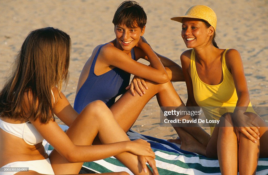 Three young women sitting on towels at beach