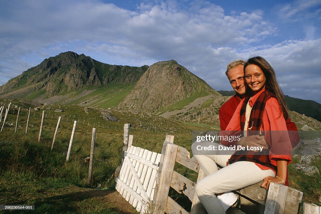 Couple sitting on fence in countryside, portrait