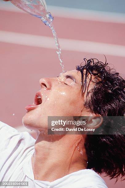 young man pouring water on forehead, close-up - refreshment bottle stock pictures, royalty-free photos & images