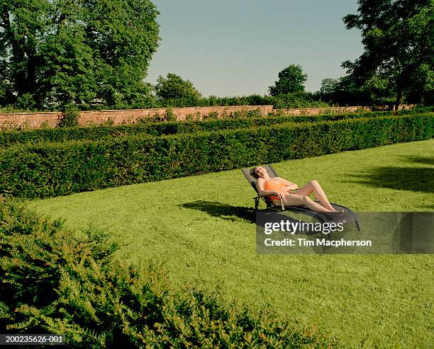 young woman relaxing on sun lounger in garden, laughing - domestic garden photos et images de collection