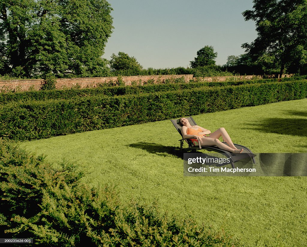Young woman relaxing on sun lounger in garden, laughing