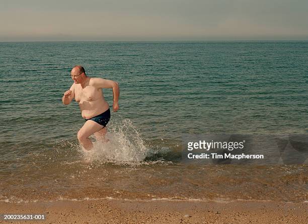 mature man on beach running in surf - fat guy on beach fotografías e imágenes de stock