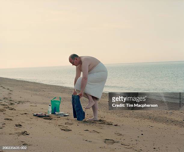 mature man dressing on beach under towel, side view - mens swimwear foto e immagini stock