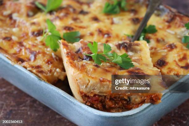 full frame image of spoon removing portion of lasagna, served from eggshell blue, ceramic serving dish, italian meal with golden surface garnished with flat leaf parsley, brown background, elevated view, focus on foreground - golden egg restaurant stock pictures, royalty-free photos & images