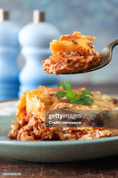 imagen de primer plano de bocado de carne picada y pasta de la porción de lasaña en un plato verde-azul, comida italiana con superficie dorada adornada con perejil de hoja plana, saleros y pimenteros, fondo azul, enfoque en primer plano - golden egg restaurant fotografías e imágenes de stock